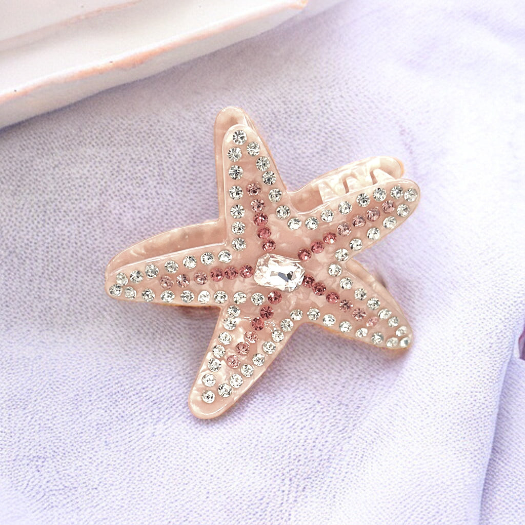 A shimmering pink starfish hair clip with five points adorned with crystal beads.
