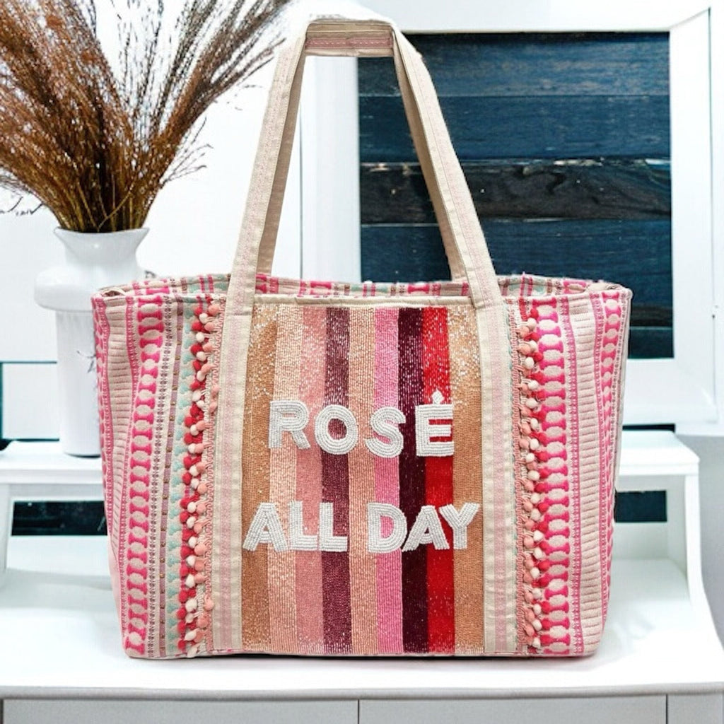 A Rose All Day tote bag in black features the phrase "Rose All Day" in a script font with shimmering gold sequins. This stylish and trendy bag is perfect for carrying your essentials on a night out or a casual day trip.
