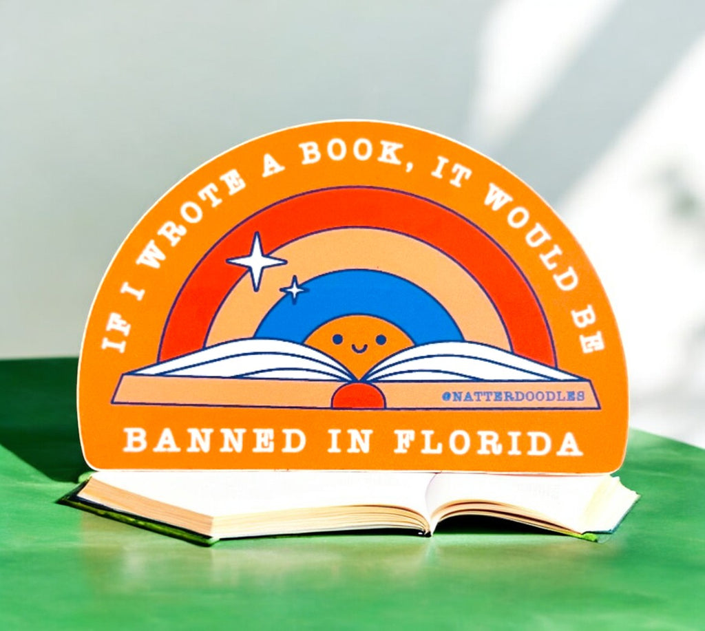 Bright and colorful sticker featuring a cheerful sun peeking out from an open book, surrounded by a retro-style rainbow. The bold text reads, 'If I wrote a book, it would be banned in Florida,' blending humor with a statement about censorship. Perfect for book lovers and advocates of free expression.