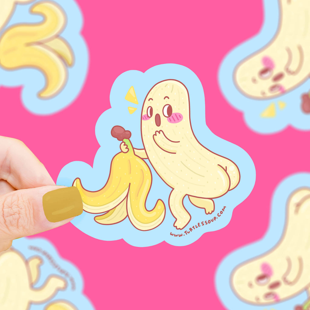 A hand holding a banana ghost sticker against a pink background.