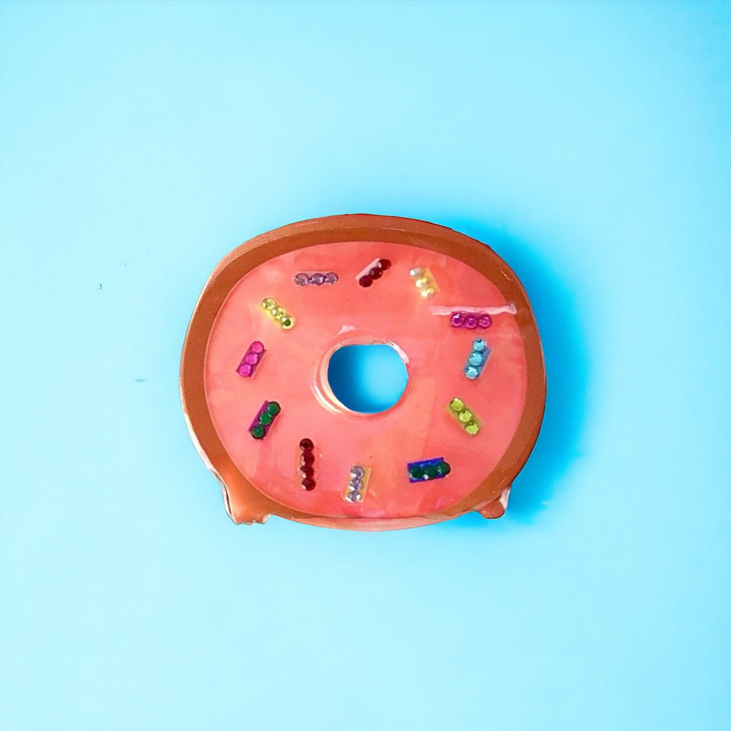 Cute and stylish pink donut hair clip, perfect for adding a touch of sweetness to any outfit.
