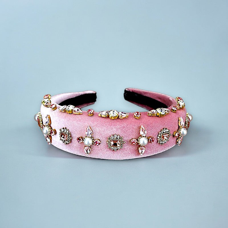 Velvet pink headband laying on its side with pearls and rhinestones with a blue background.