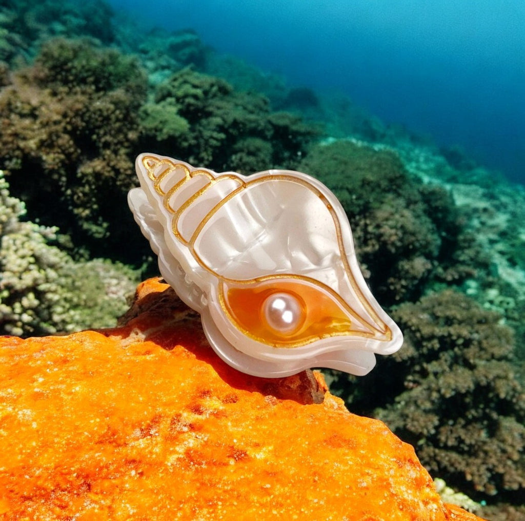 Elegant mini hair clip shaped like a seashell, featuring a pearl accent and gold details with orange highlights.