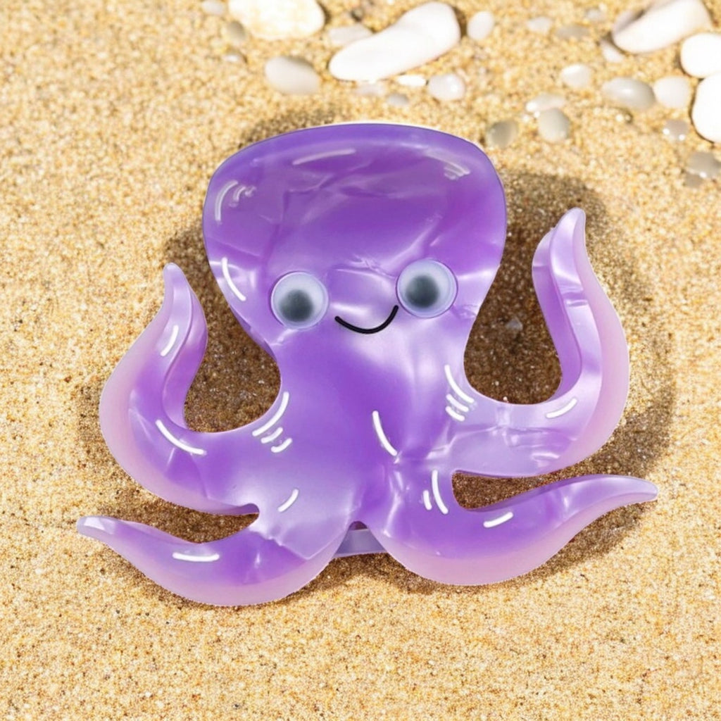 Purple octopus hair clip on sand with shells.