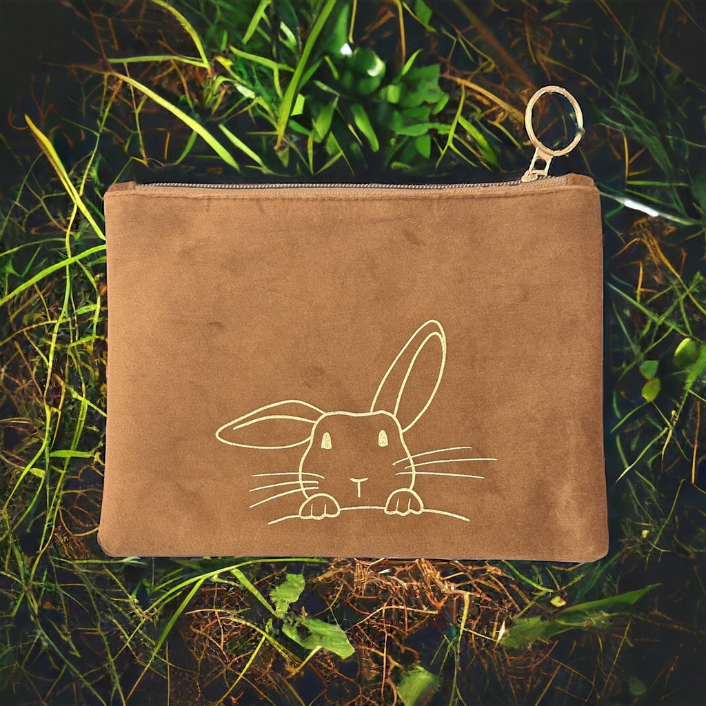 Close up of a tan colored bunny face shaped soft suede pouch with bunny ears adorned with large gold colored studs on a yellow background.
