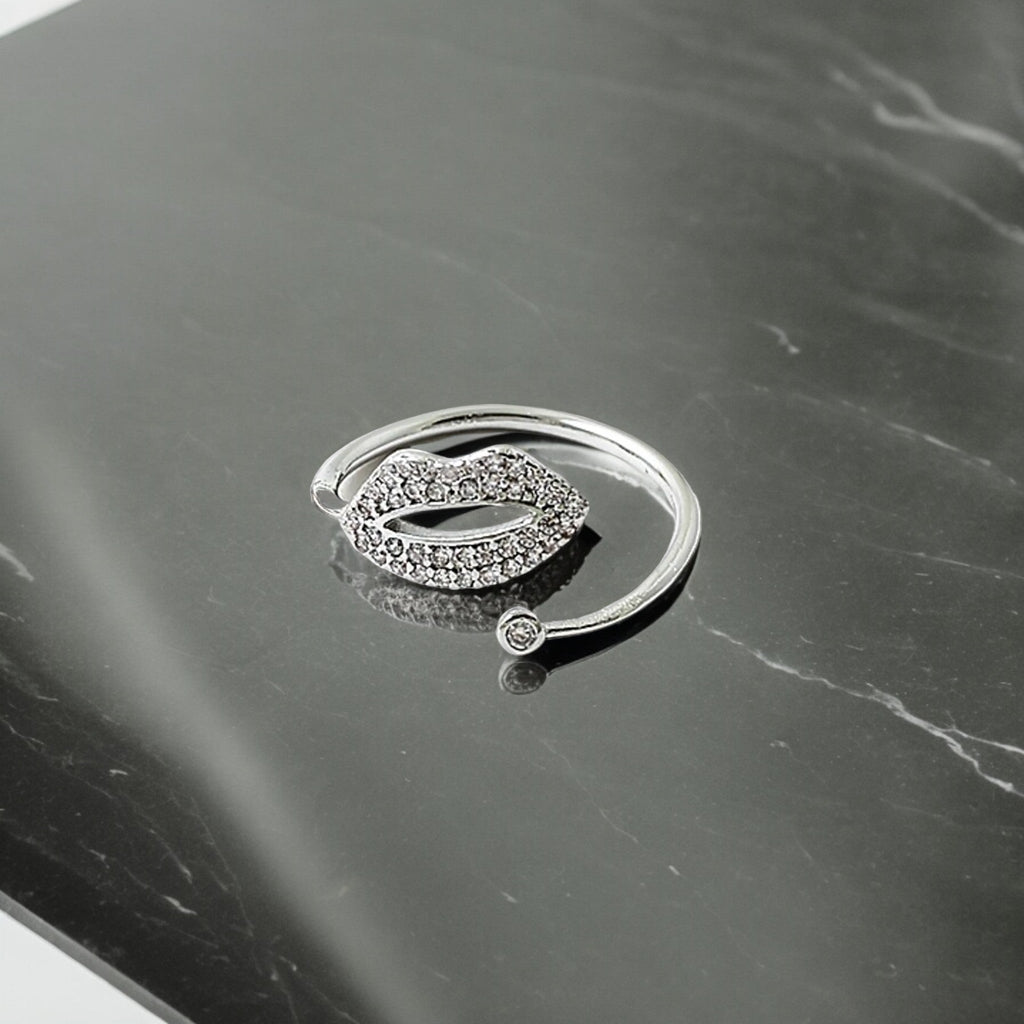 Silver ring with lips on it resting on a marble surface.