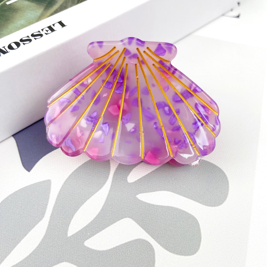 Purple shell hair clip with gold accents on gray background.